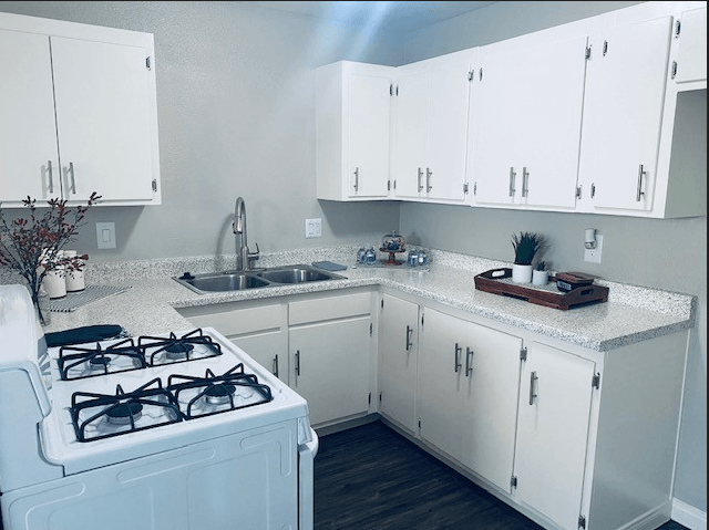 A white kitchen with a stove, sink, and cabinets.